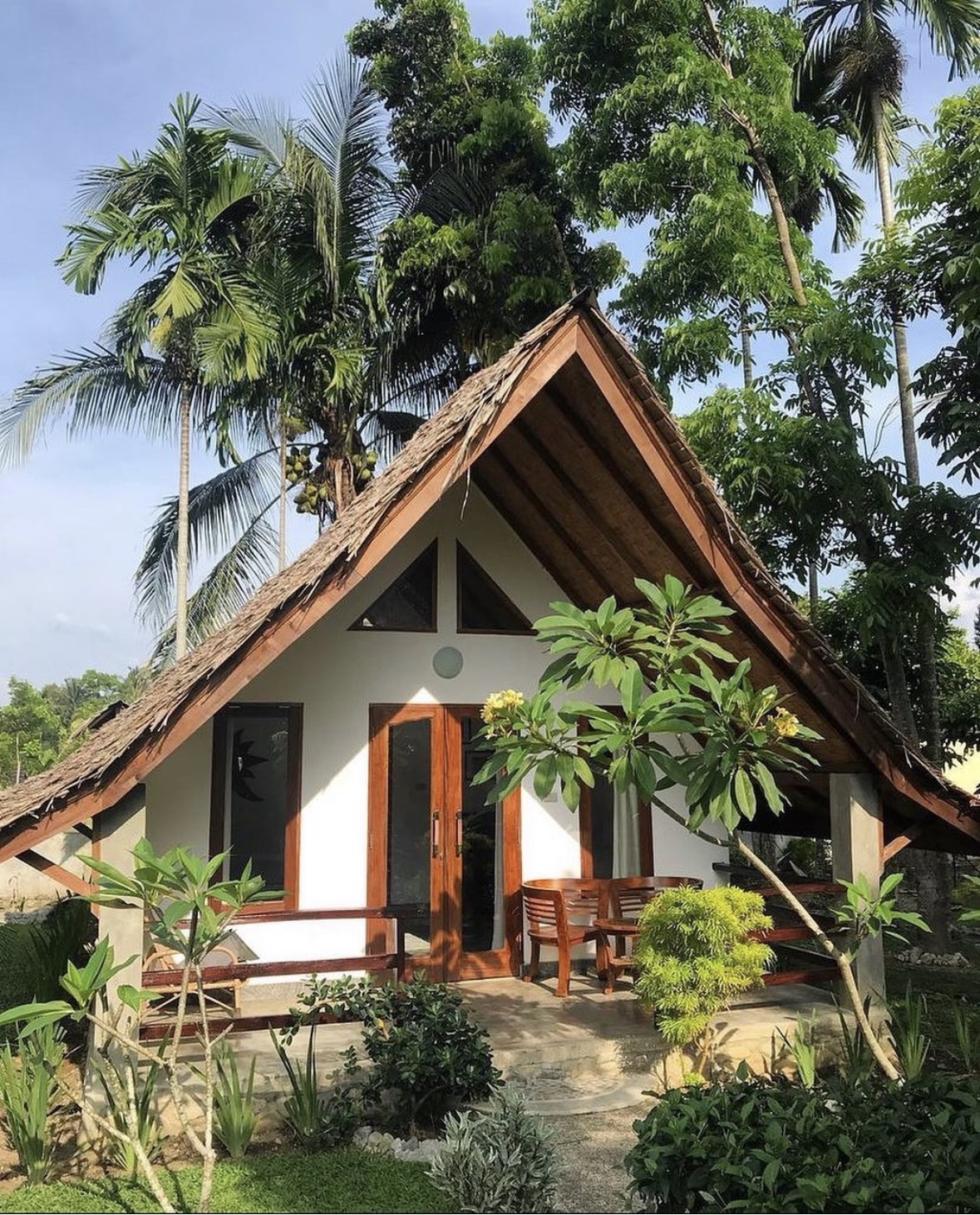 Thatched-roof bungalow exterior with terrace and frangipani garden at Villa Paradise guest house in Bukit Lawang, North Sumatra